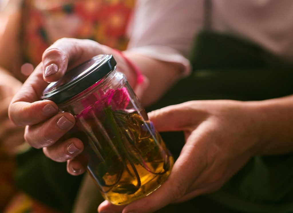 a close up on a pair of hands gently holding a small jar with a black lid. inside the jar are flowers and sugar water.